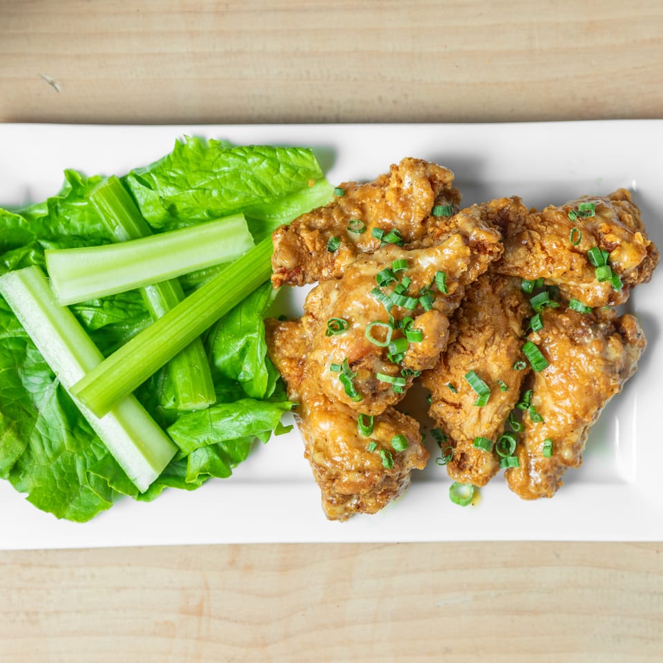 Crispy sauced chicken wings garnished with green onions, served alongside lettuce leaves and celery sticks on a white platter.