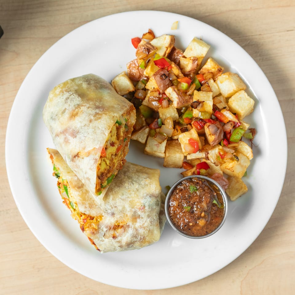 Plate of stuffed flatbreads with seasoned roasted potatoes, peppers, onions, and a side of dipping sauce.